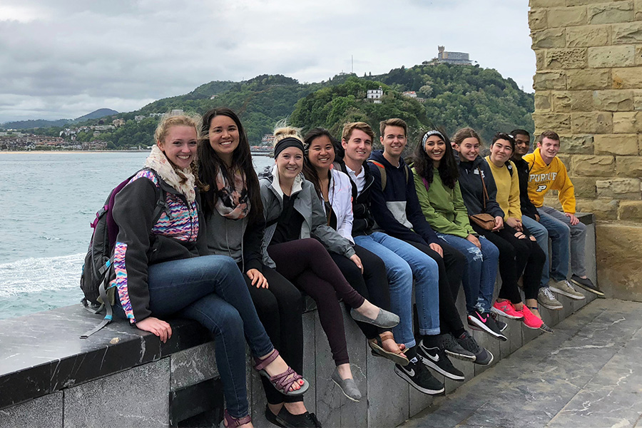 Students seated together on a wall next to a lake