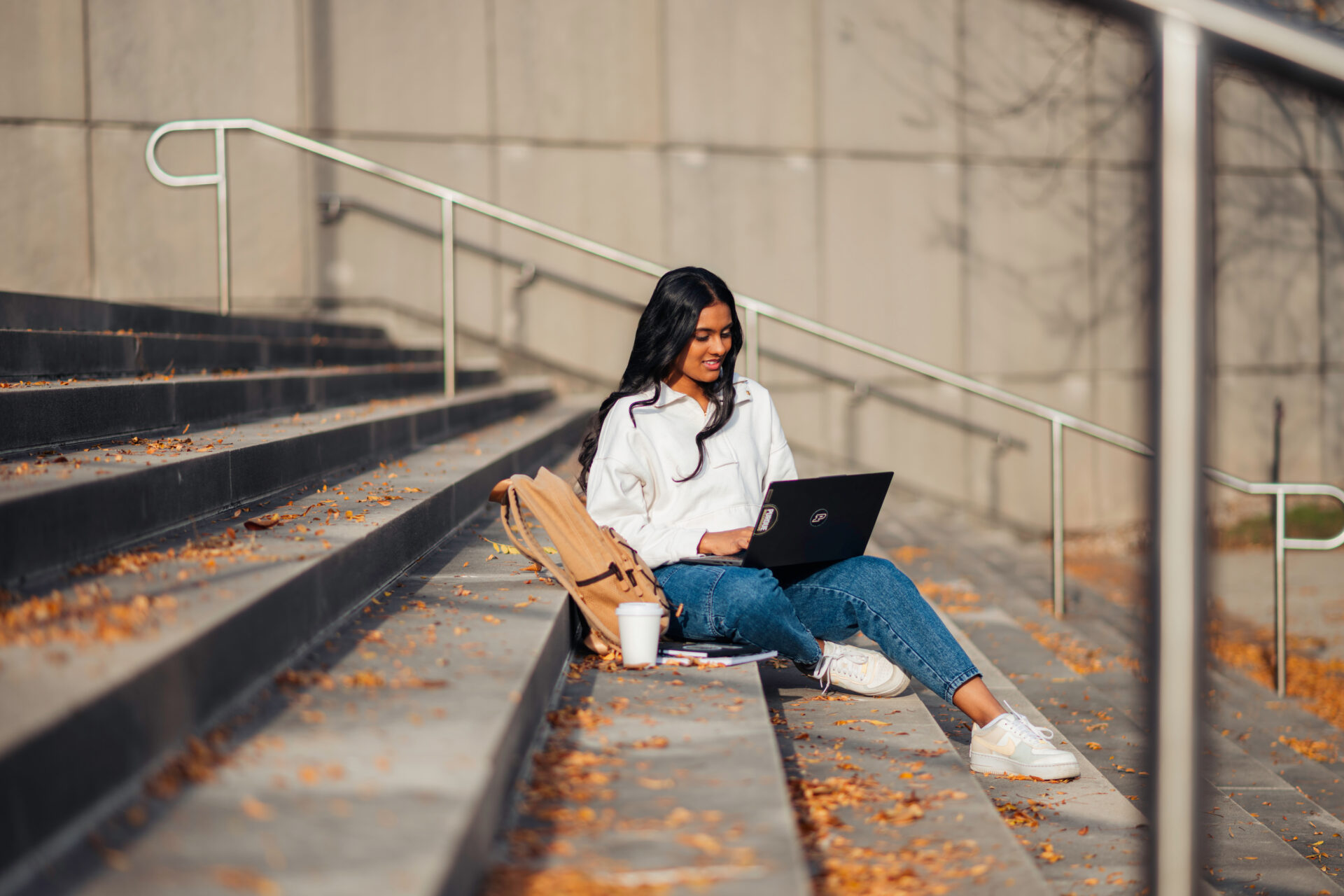 Female sitting on steps outside working on her laptop.