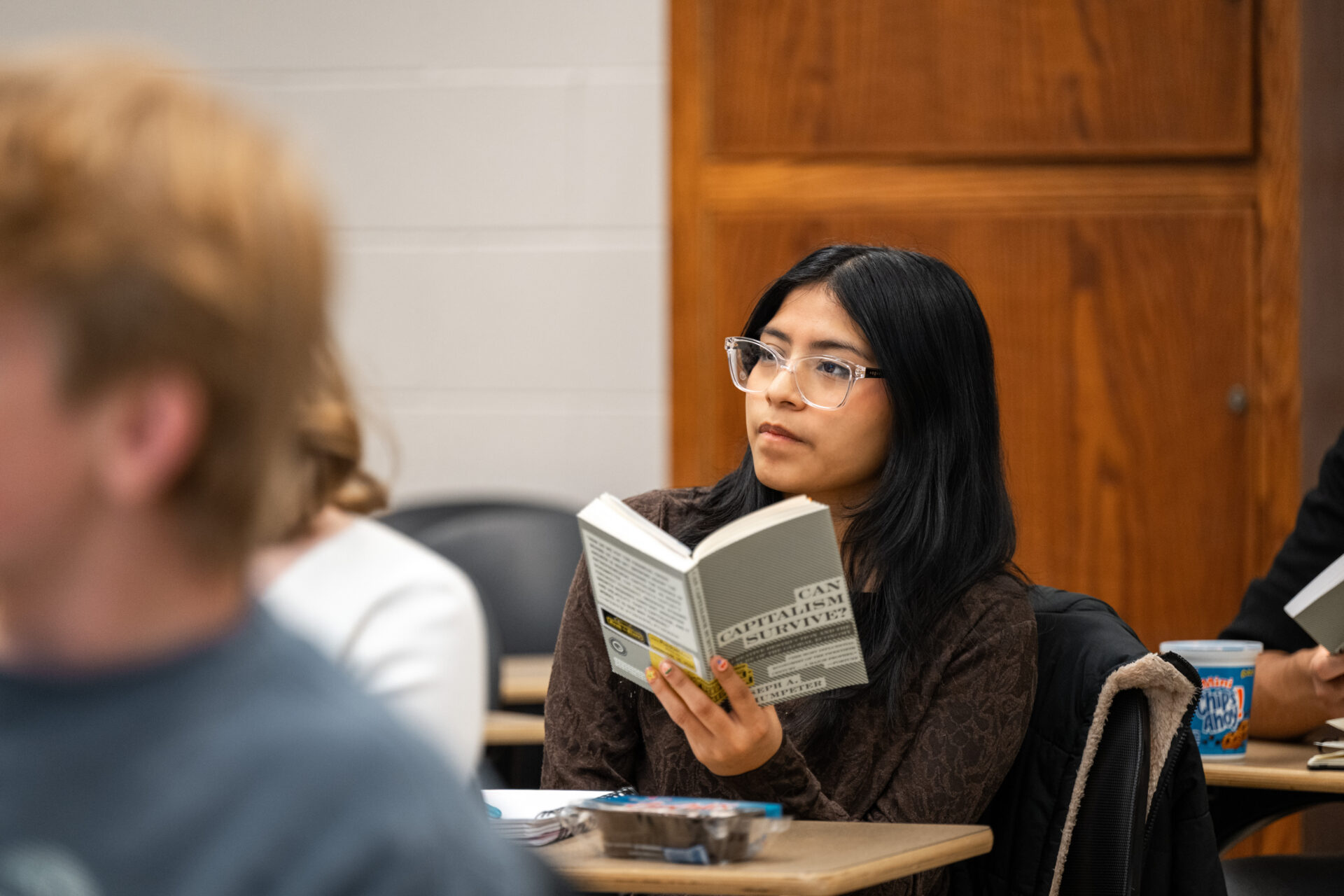 Female student in a classroom holding in her hand an open book.