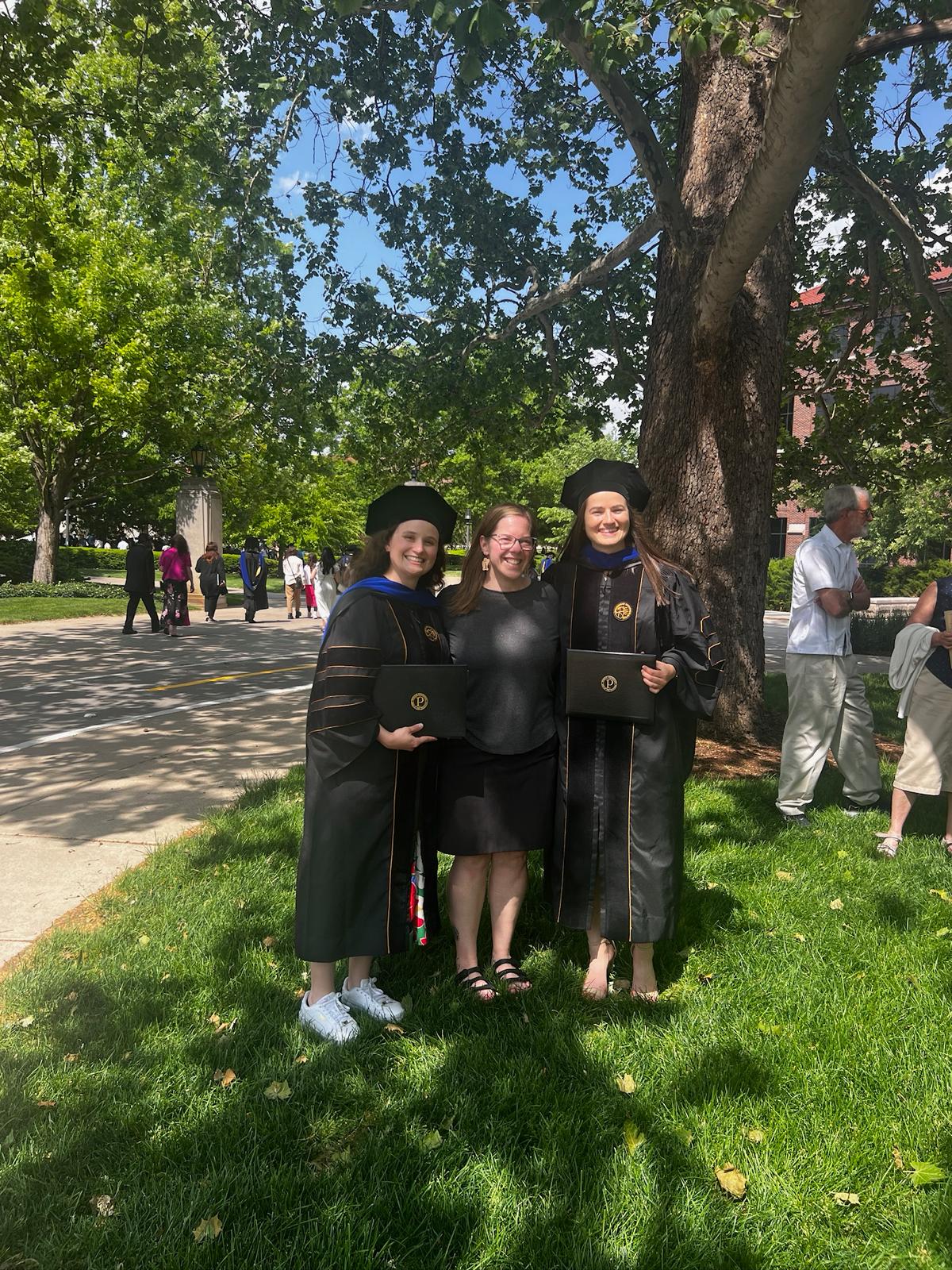 Two graduates standing with person