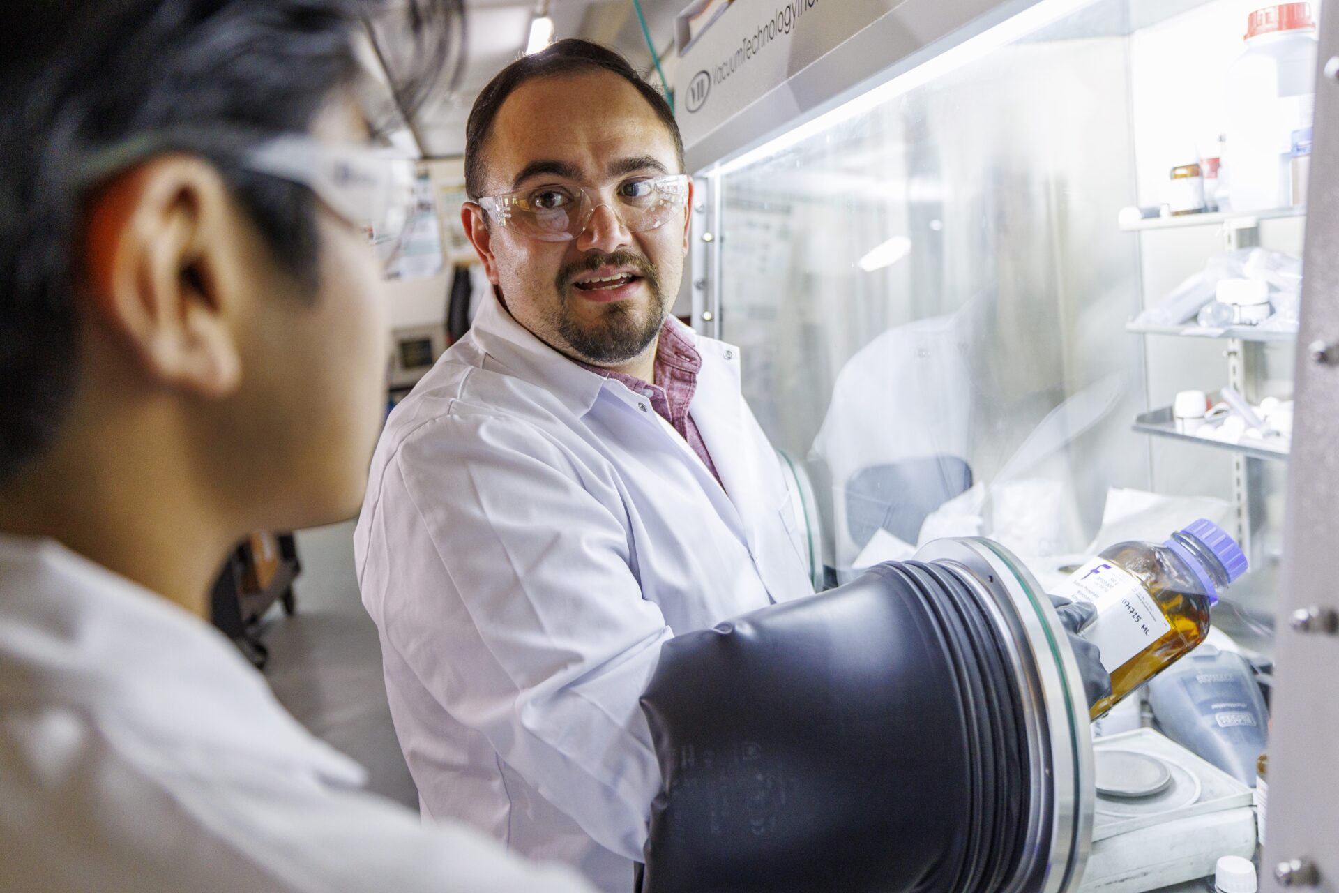 Two people wearing white coats and safety glasses working in a lab together.