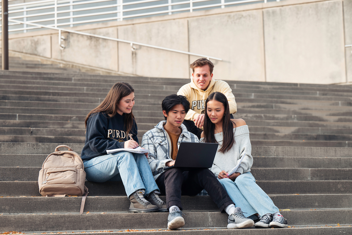 Four students sitting together on a staircase looking at a laptop