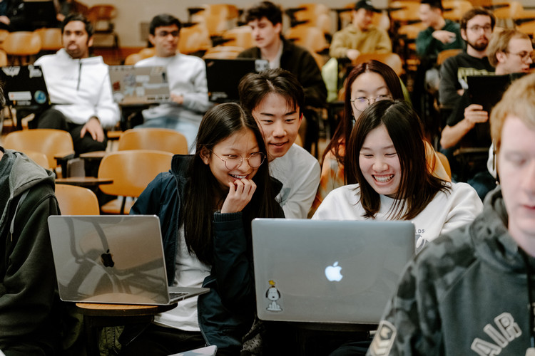 Smiling students in a theater-style classroom looking at their laptops