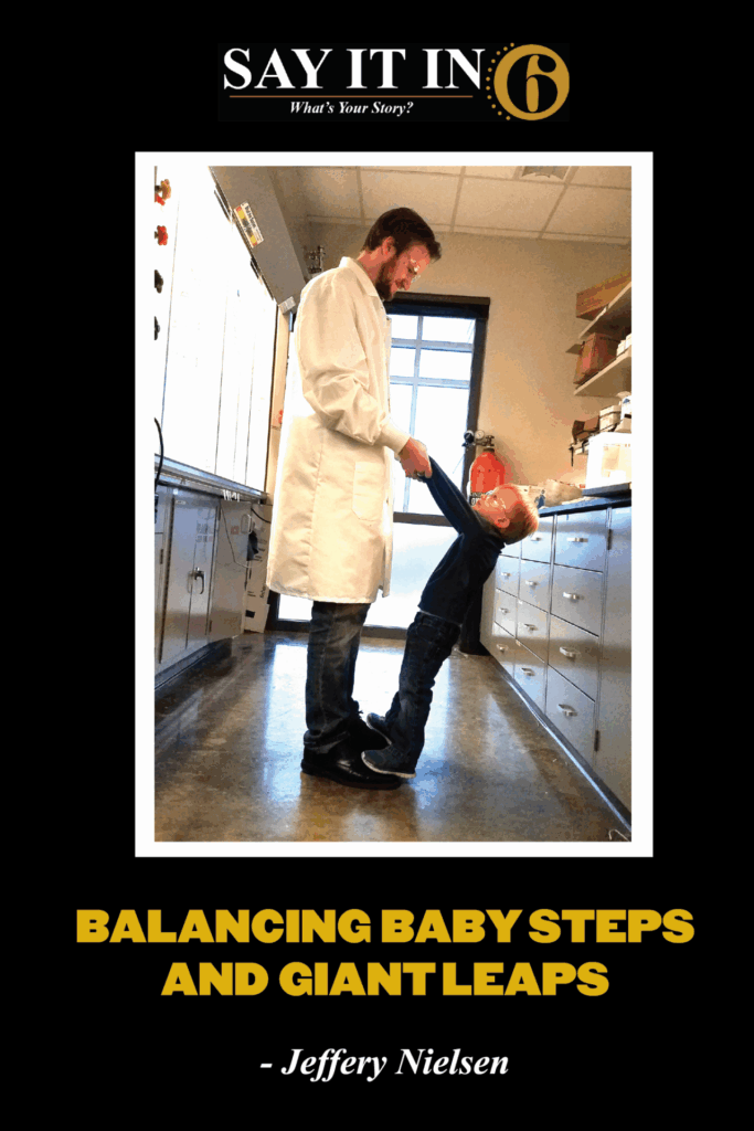 Man in white lab coat holding the hands of his son who is standing on his father's feet with the caption," balancing baby steps and giant leaps."