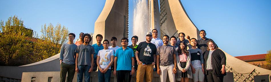 A group of people pose together in front of a fountain on Purdue's campus