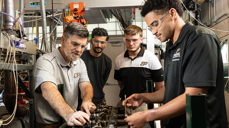 A Purdue professor works with three students in a lab, all wearing lab goggles.