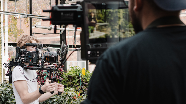 Videographer filming with a professional camera rig in greenhouse.