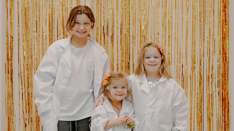 Children wearing lab coats in front of yellow streamers