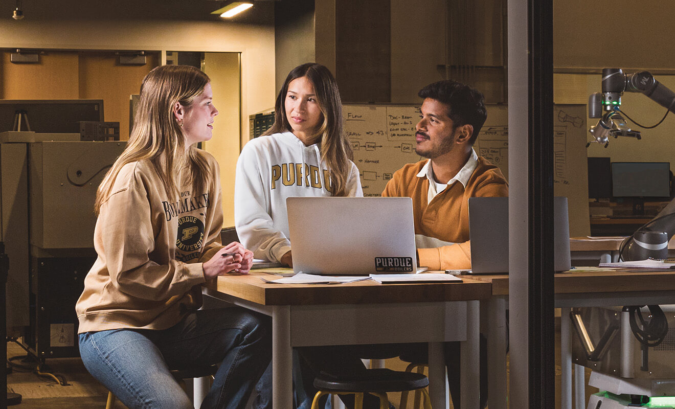Purdue students collaborating around a laptop in a lab.