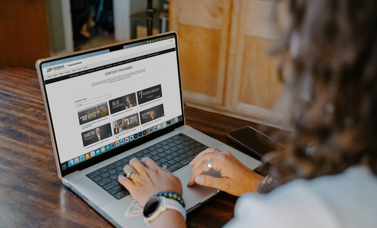 A person typing on a laptop displaying the Purdue Brand Studio Content Packages web page.