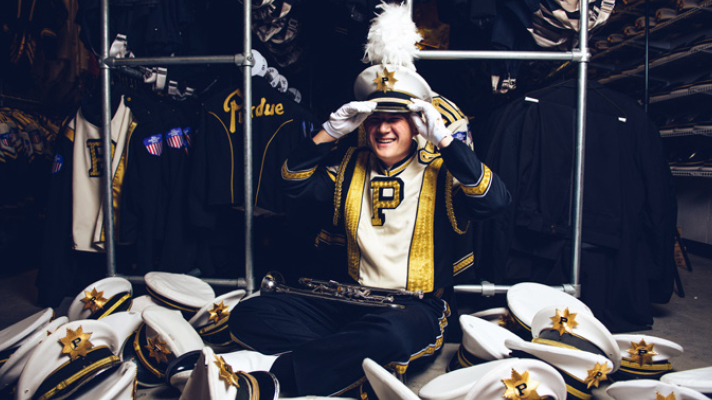 Purdue marching band member surrounded by uniform hats.