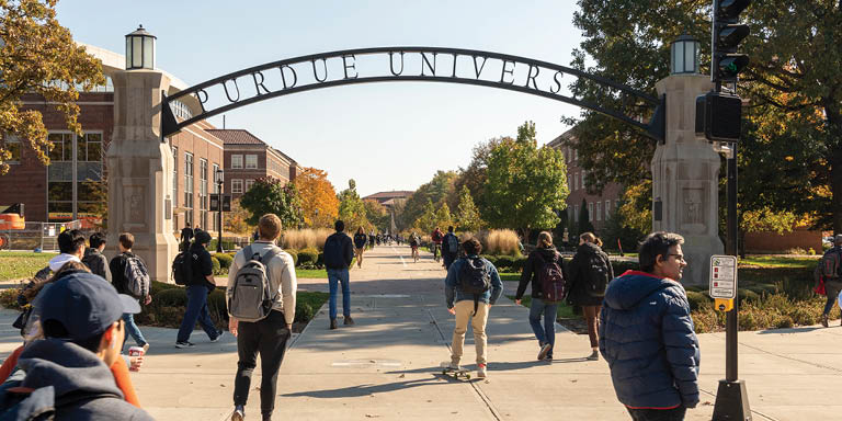 Students walking under the Purdue gateway arch on a sunny autumn day