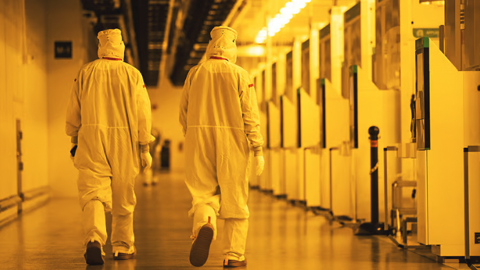 Workers in hazmat suits walking down cleanroom corridor.