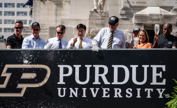 Purdue officials celebrating behind a university sign.