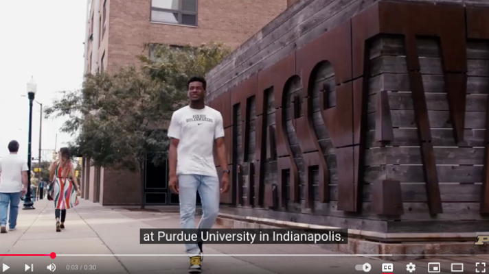Purdue student walking near a Mass Ave landmark sign.