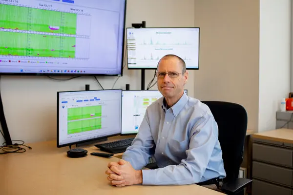 man sitting at a desk with multiple computer screens displaying data graphs