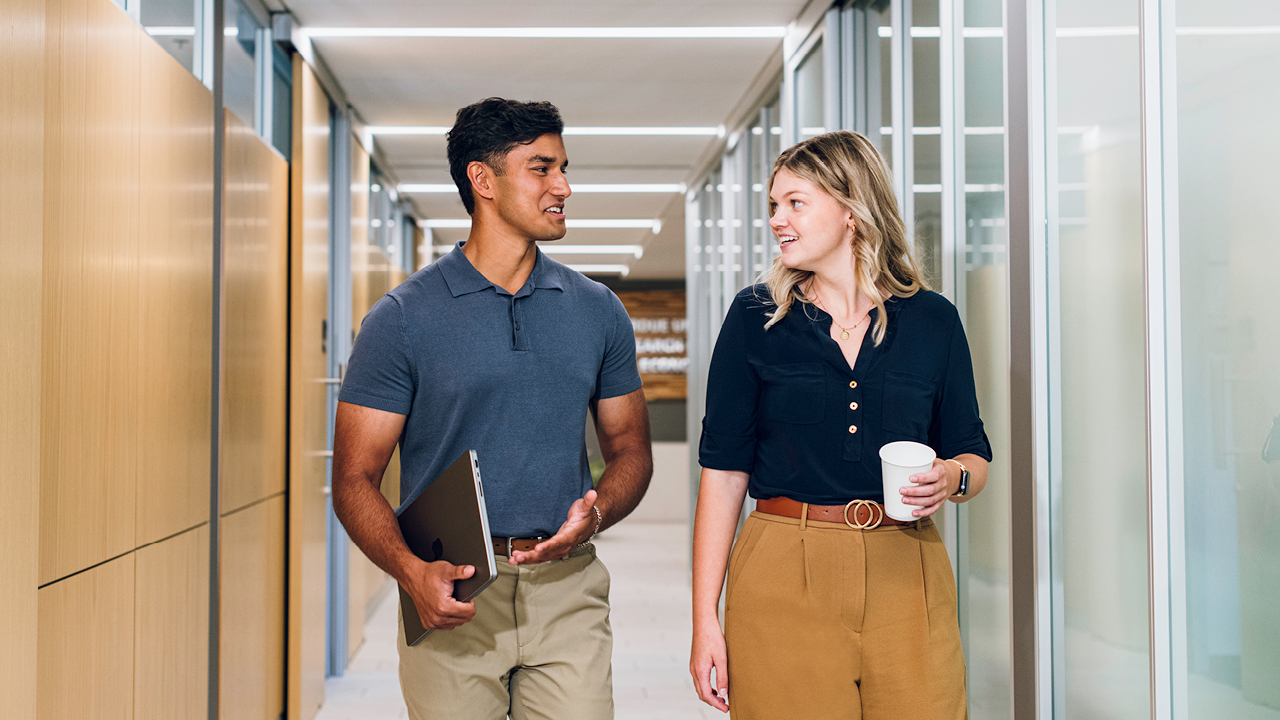 Male and female walking down hallway with glass walls