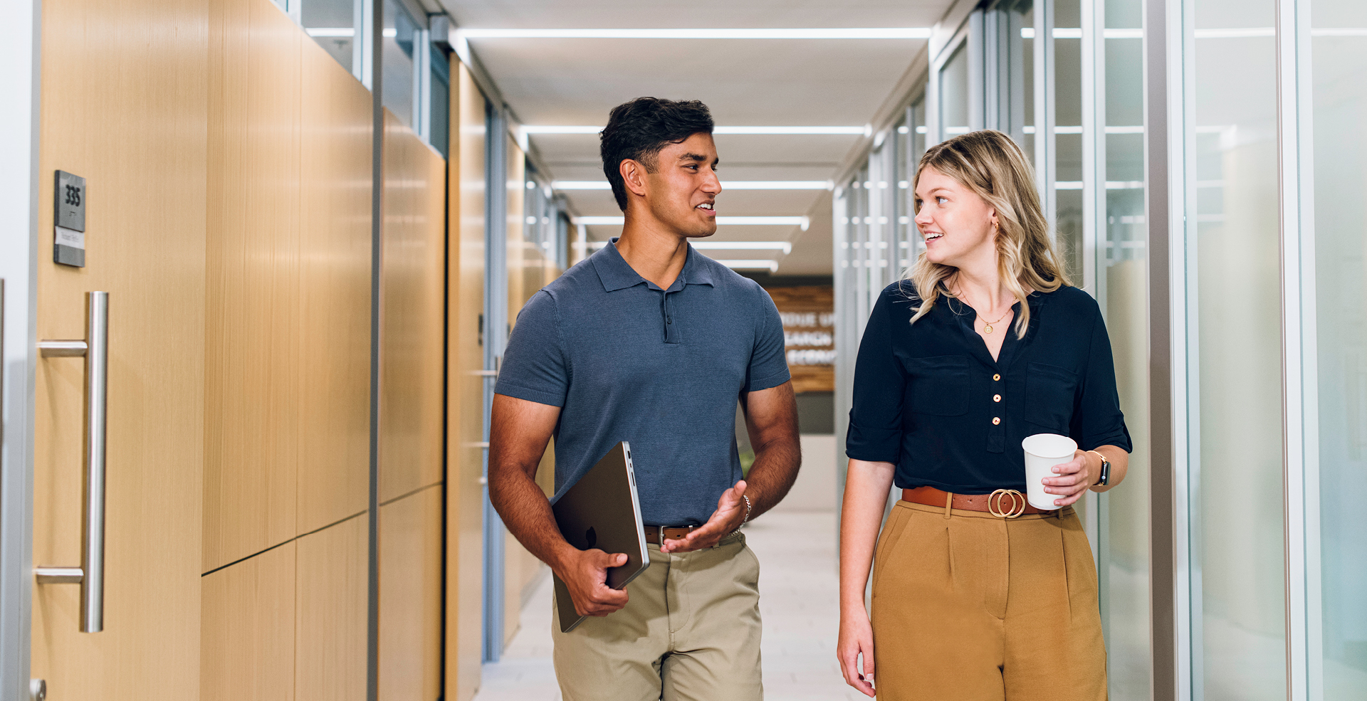 Male and female walking down hallway with glass walls