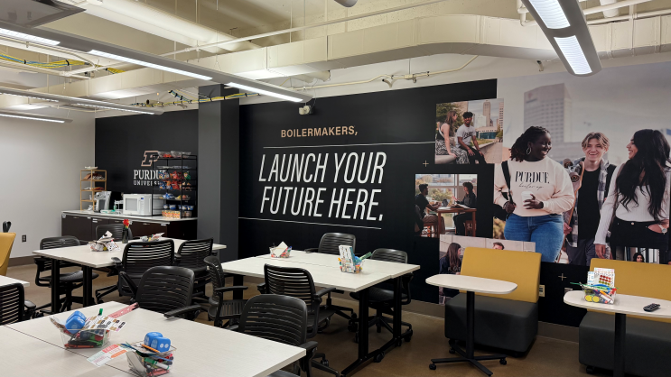 Purdue University Indianapolis Launch Pad workspace with tables, chairs, bright lighting, and a wall featuring the text “Boilermakers, Launch Your Future Here” with Purdue branding and photos.