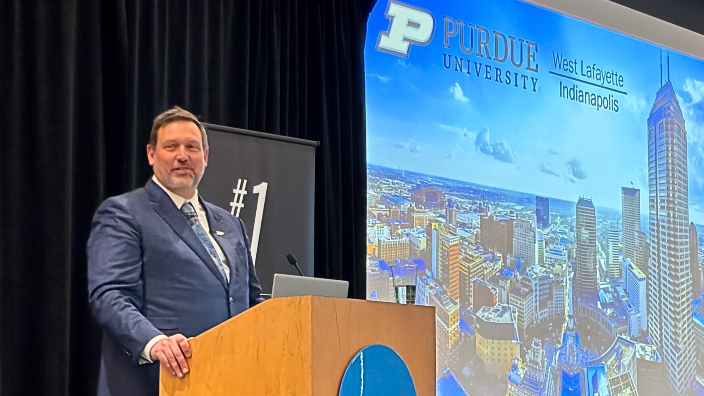 A university leader speaks at an event, applauding faculty and staff contributions and discussing expanded research and industry opportunities for Purdue students in Indianapolis.