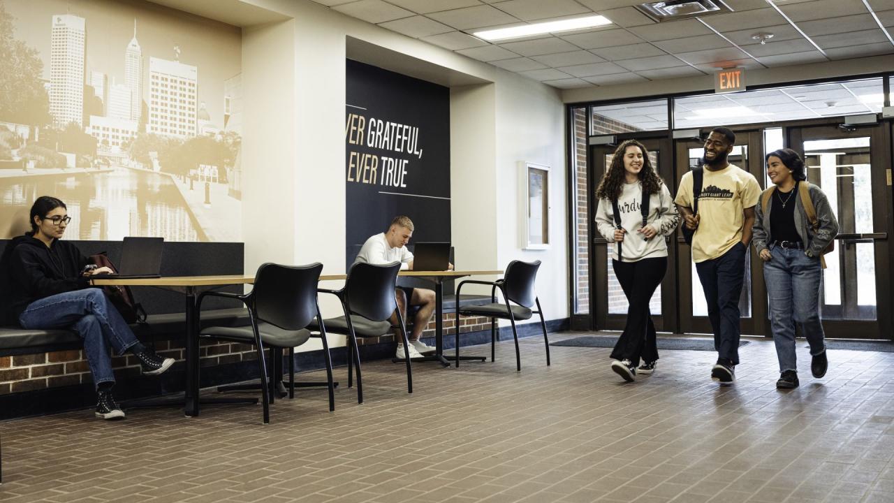 Three students wearing backpacks walk side by side down a Purdue branded hallway