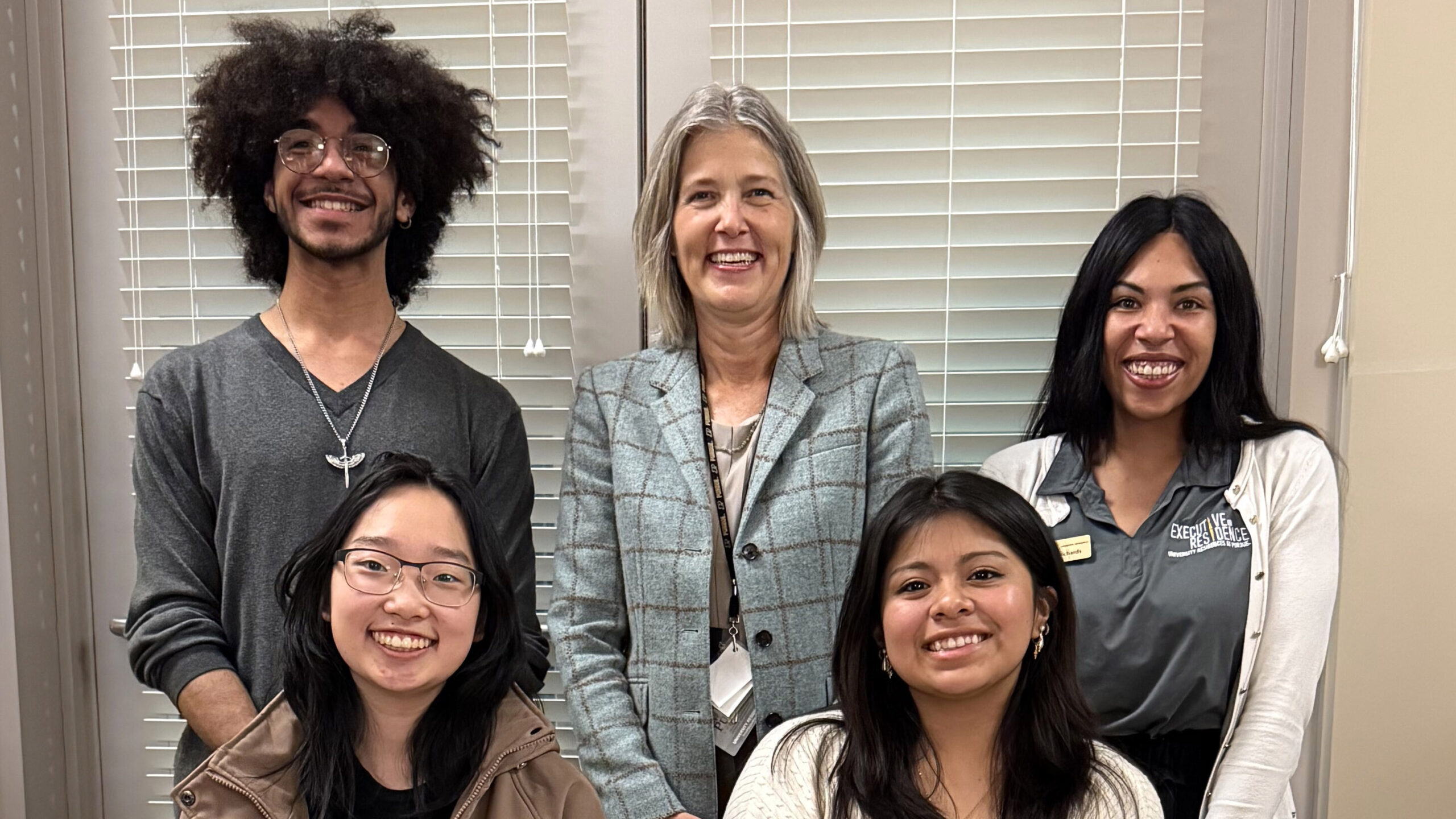 A student, Purdue aluma, and academic advisor standing behind two students in chairs.