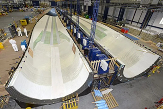 Large composite structures being manufactured on an industrial factory floor, showing automated layup and production of aerospace-scale components.