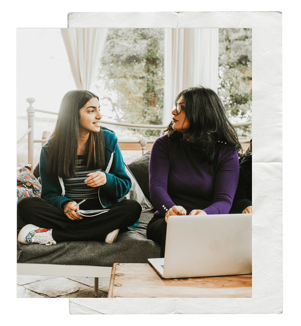 Teenage girl and mother conversing with one another in front of open laptop.