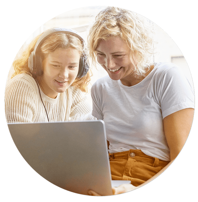 Teenage girl wearing headphones and mother watching video on laptop.