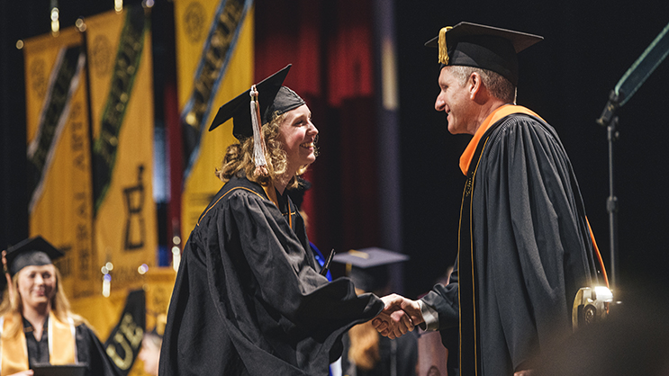 Graduate shaking hands with faculty after receiving diploma on stage