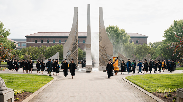 Purdue graduates walking beside the engineering fountain on the way to commencement