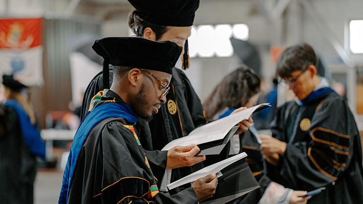 Graduates reading program while waiting in the armory before commencement