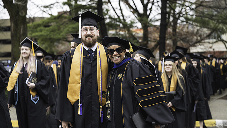 Graduate and faculty posing for a photo while walking to commencement