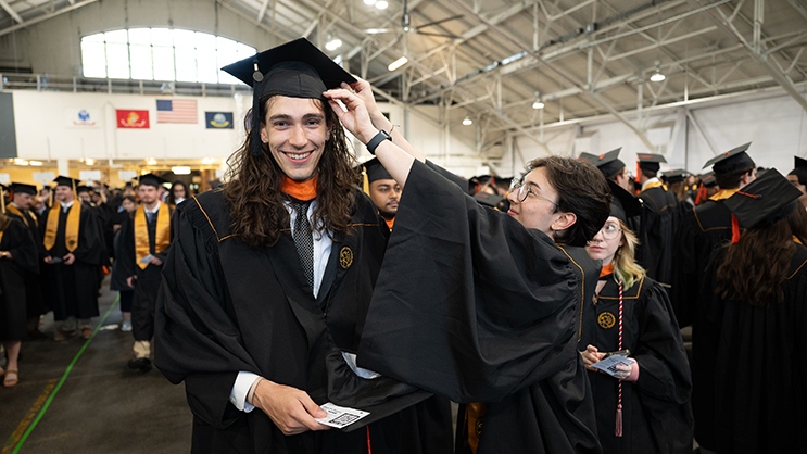 Graduate inside the armory getting his mortar board adjusted