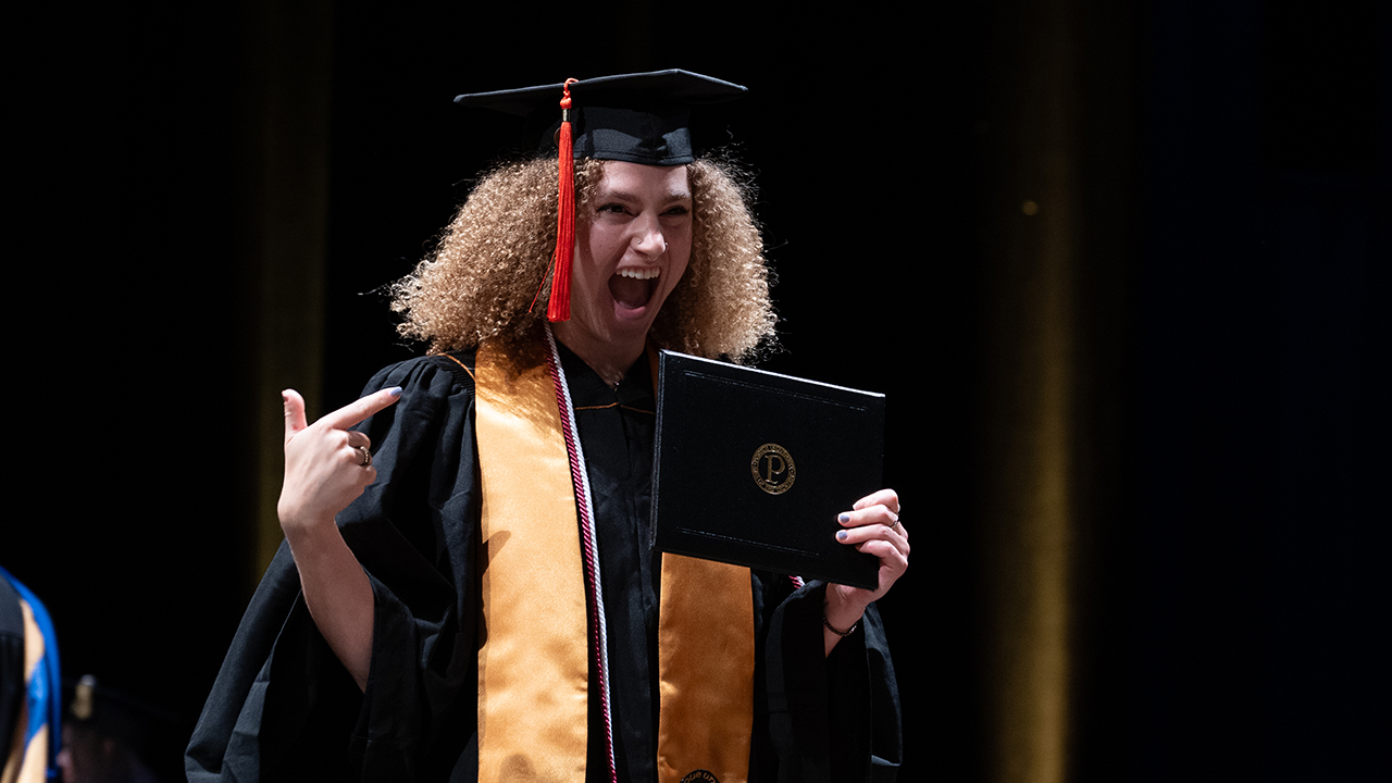 Graduate pointing to her diploma on stage with excitement
