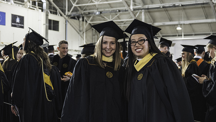 Two graduates posing for a photo while waiting in armory before commencement