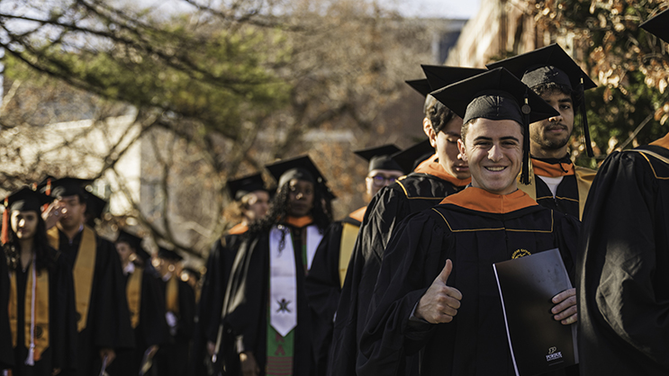 Graduates lined up outside for commencement with someone giving a thumbs up 