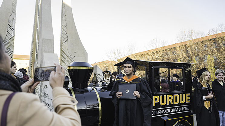 Graduate holding diploma, posing in front of engineering fountain with the extra special train in the background