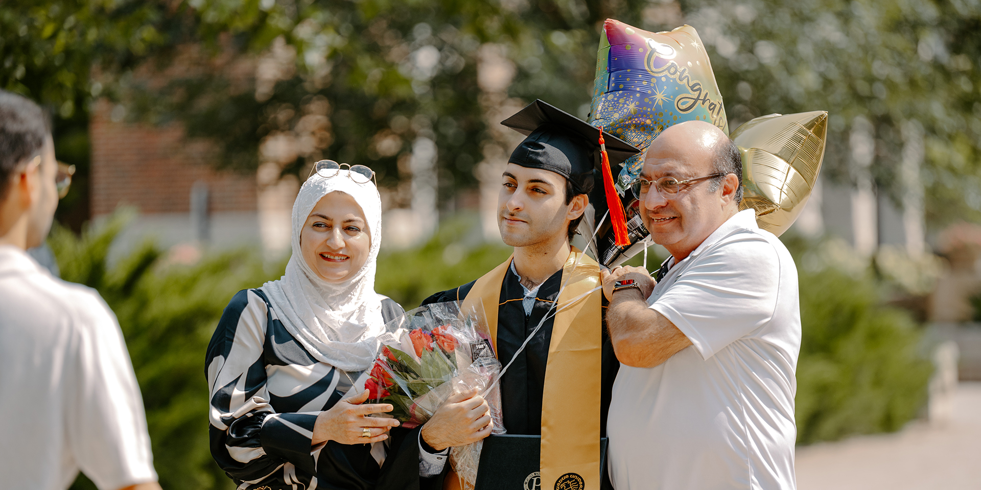 Family posing with Purdue graduate holding balloons and flowers