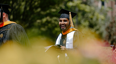 Smiling graduate seen through blurred plants