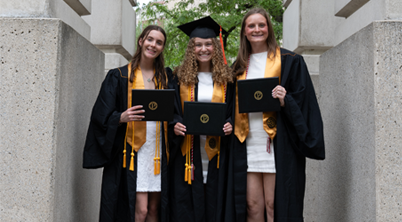 Three smiling graduates pose with their diplomas after graduation