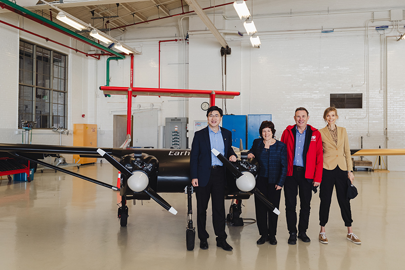 Four people standing next to a large fixed-wing drone inside a large interior space.