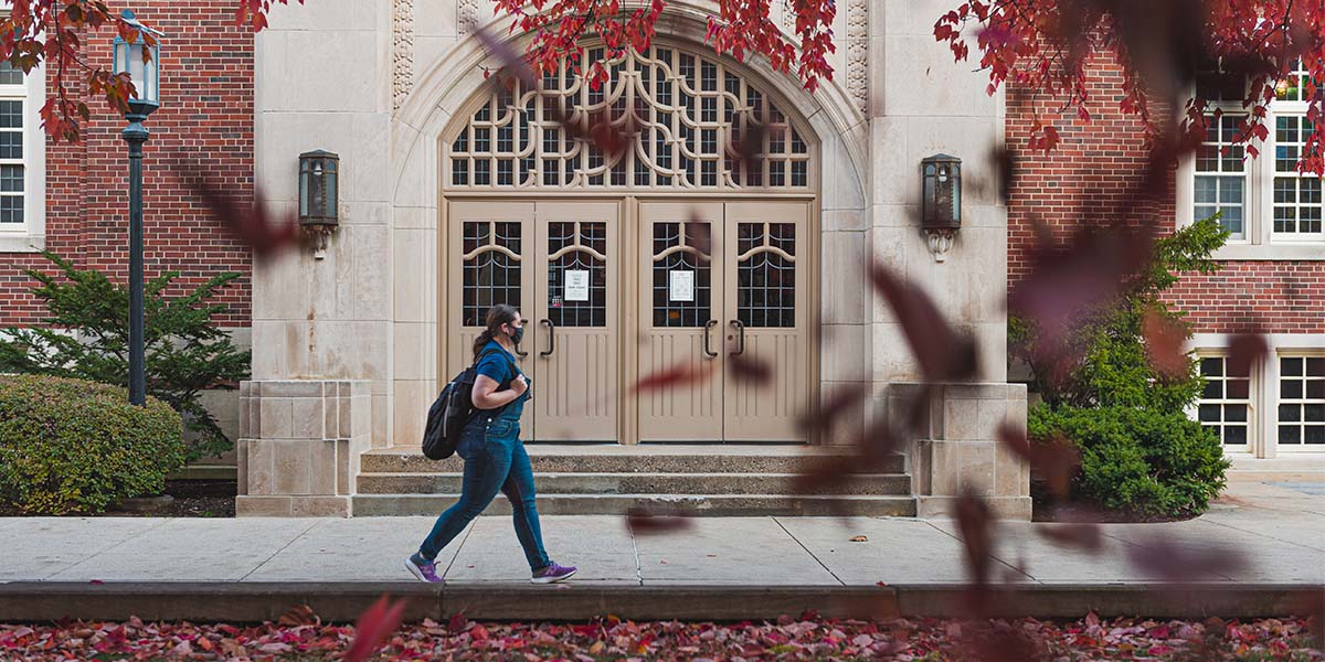student walking on campus as red leaves fall during the autumn season