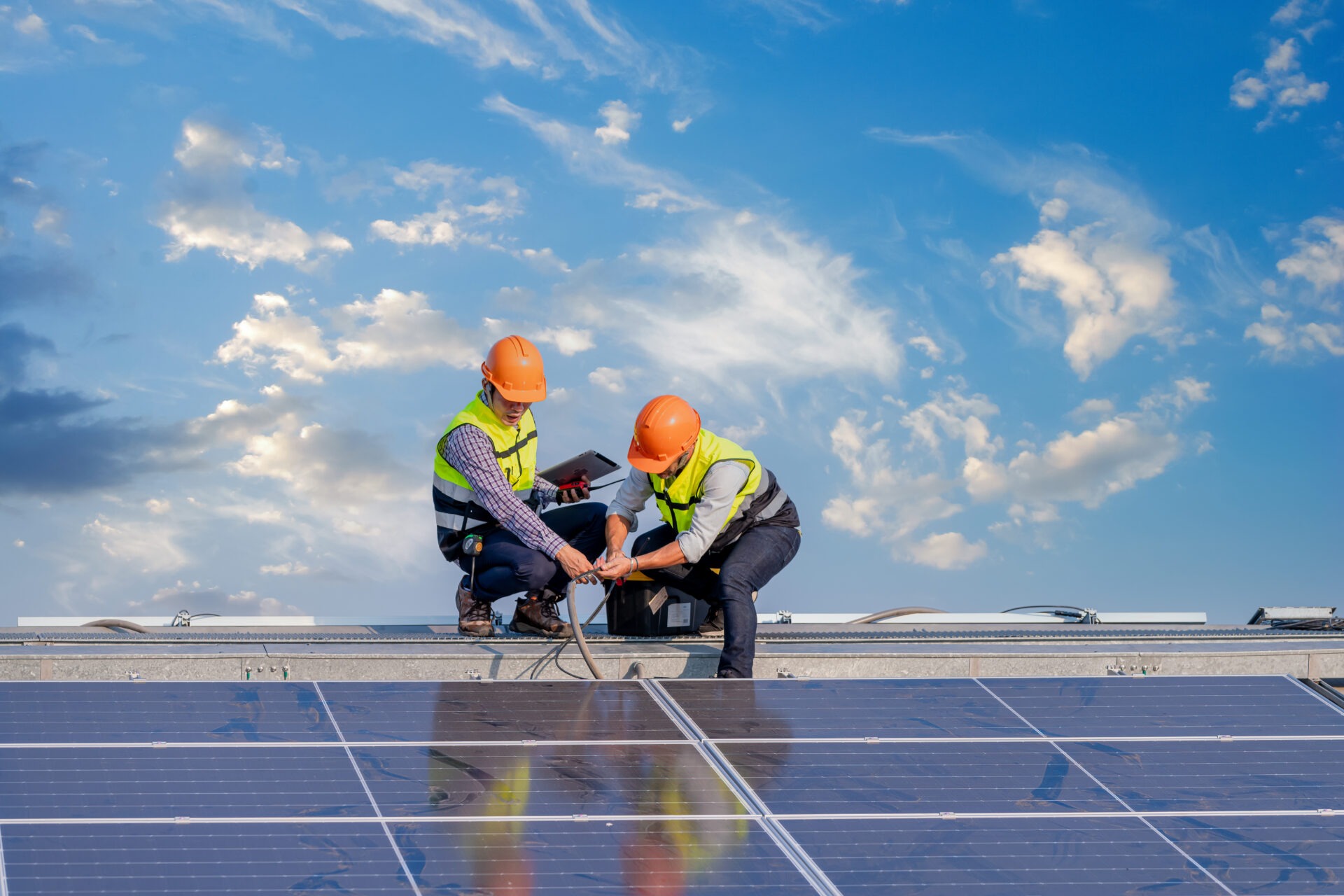 Two engineers in hard hats inspecting rooftop solar panels.