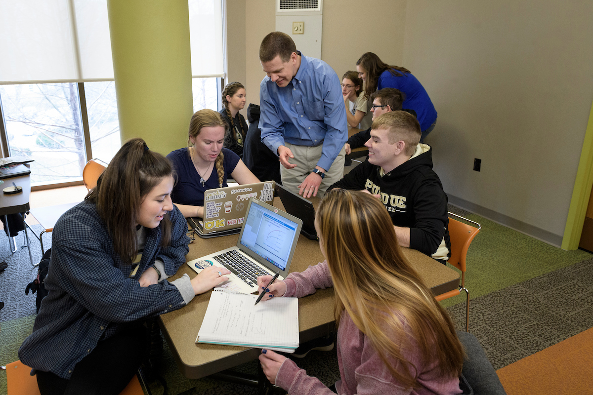 Pictured: Students in a classroom work closely with their professor, all of them on laptops.