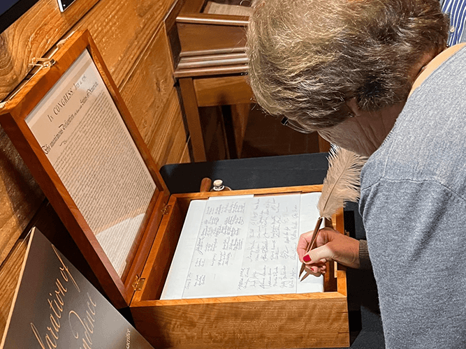 A visitor signs the interactive Declaration of Independence scroll with a replica quill pen