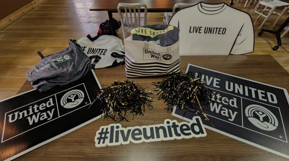United Way of Greater Lafayette shirts, signs, and pom-poms displayed on a table with a #liveunited sign