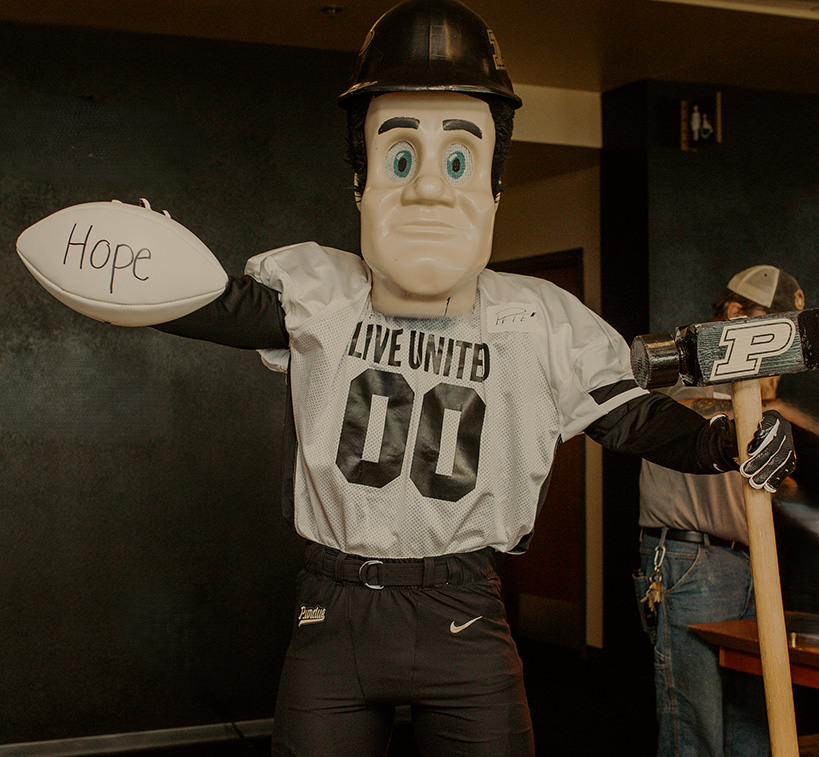 Purdue Pete in a Live United jersey holding a football with the word Hope written on it