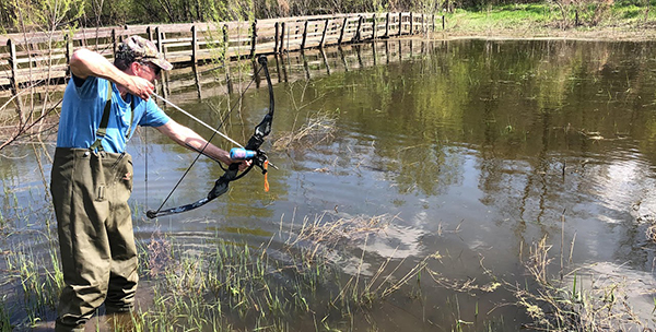 Man with wades in lake bowfishing, Purdue Bowfishing Research.