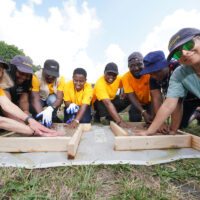 2023 Mandela Fellows bending down with hands in soil boxes.